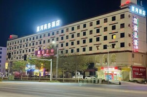 Un hotel de varios pisos con señalización llamativa, una entrada cubierta y vista a la calle con semáforos.