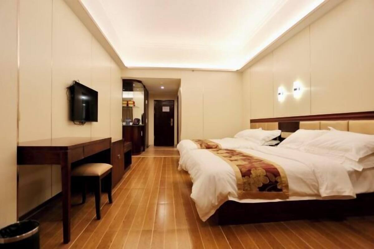 A hotel room with a large bed, a desk, a chair, a television, and a trash bin.