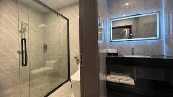 Un baño moderno con ducha envuelta en cristal, inodoro blanco y lavamanos negro con espejo superior.