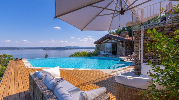 A wooden deck with wicker furniture and a pool overlooking a scenic view of the sea. - Paradis Relais Pool View EV Recharge (Belgirate)