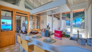 A modern kitchen with a central island, wooden cabinets, and a stone wall. - Paradis Relais Pool View EV Recharge (Belgirate)