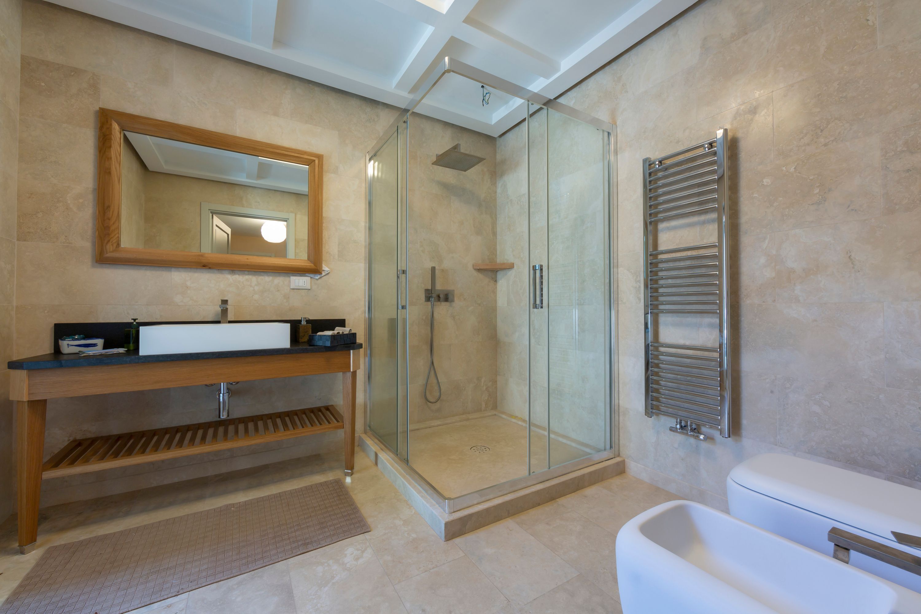 A modern bathroom with a glass-enclosed shower, a wooden vanity with a mirror, and a white toilet.