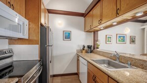 A kitchen with wooden cabinets, a stainless steel refrigerator, a microwave, an oven, a dishwasher, and granite countertops. - Kiahuna Plantation Resort 190 Ocean View 1 Bedroom (Koloa)