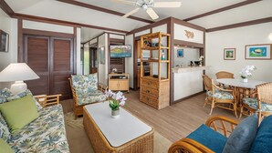A cozy living area with a sofa, coffee table, and wicker furniture. There is a dining table with chairs, a kitchen area, and a ceiling fan. - Kiahuna Plantation Resort 190 Ocean View 1 Bedroom (Koloa)