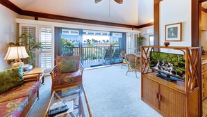 Un salon spacieux avec un ventilateur de plafond, un canapé, une table basse et un téléviseur posé sur un meuble en bois.