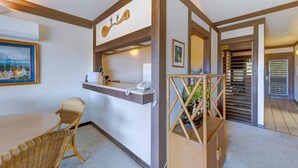 Un espace d’accueil comprenant un comptoir, des fauteuils en osier, un tableau encadré et un escalier en bois.