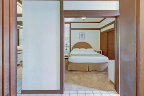 Un dormitorio con cama, mesita de noche, lámpara, ventana con persianas y puerta de madera.