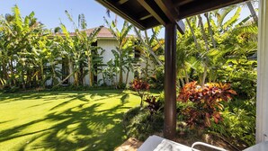 A covered patio area with a lawn, surrounded by tropical plants and a building in the background. - Kiahuna Plantation Resort Ocean View 1 Bedroom (Koloa)