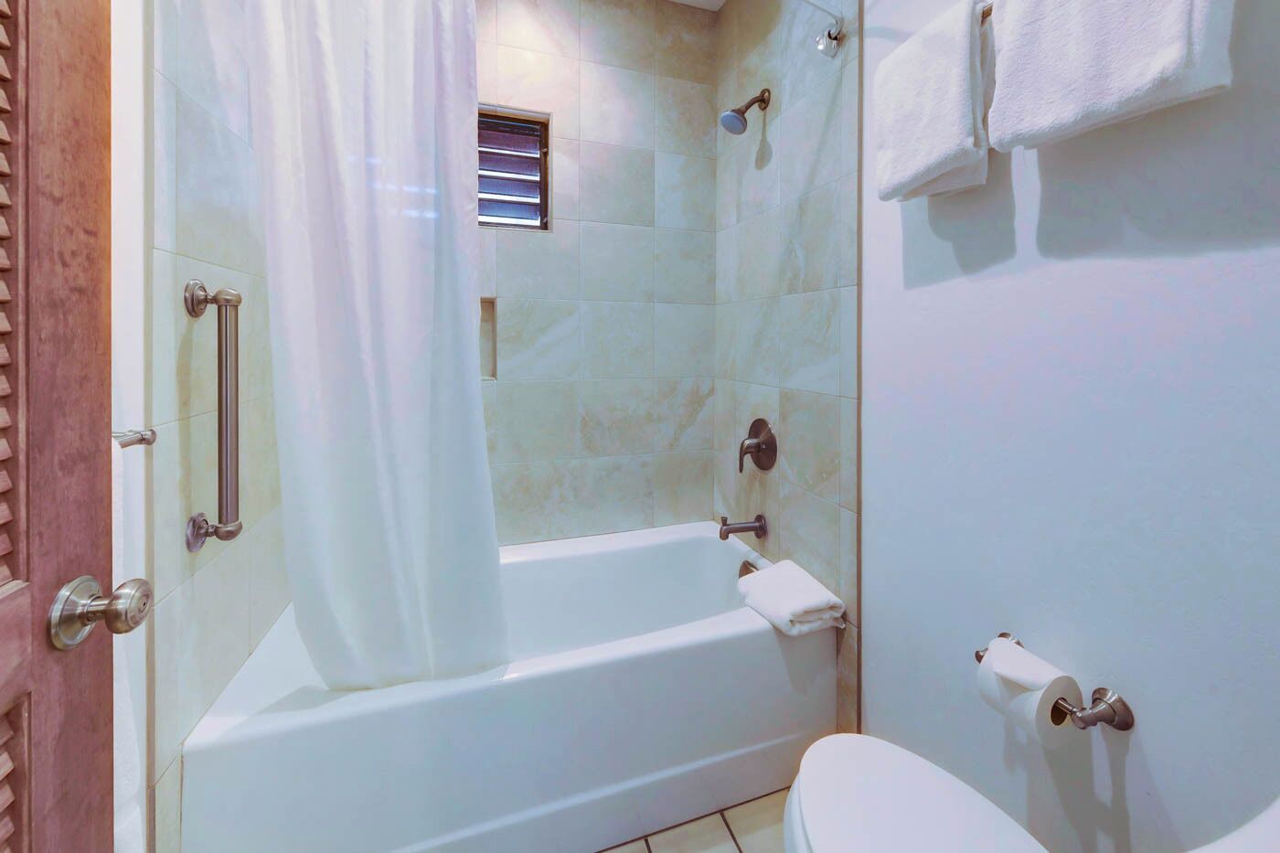 A bathroom with a bathtub, toilet, shower curtain, and a small window.