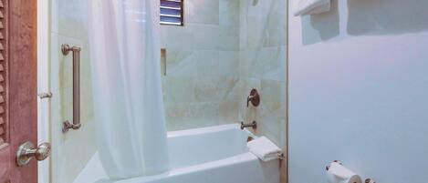 A bathroom with a bathtub, toilet, shower curtain, and a small window.