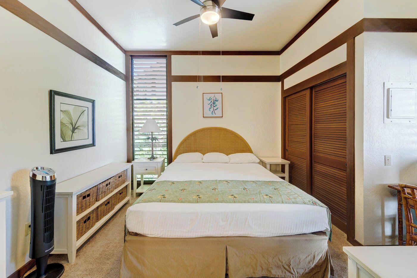 Quarto com cama, ventoinha no teto, mesa de cabeceira, abajur, aquecedor, janela com persianas, porta e quadro na parede.