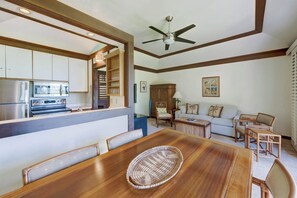Una cocina moderna con electrodomésticos integrados, un comedor con mesa y sillas de madera, un ventilador de techo y una sala de estar con sofá y cojines decorativos.