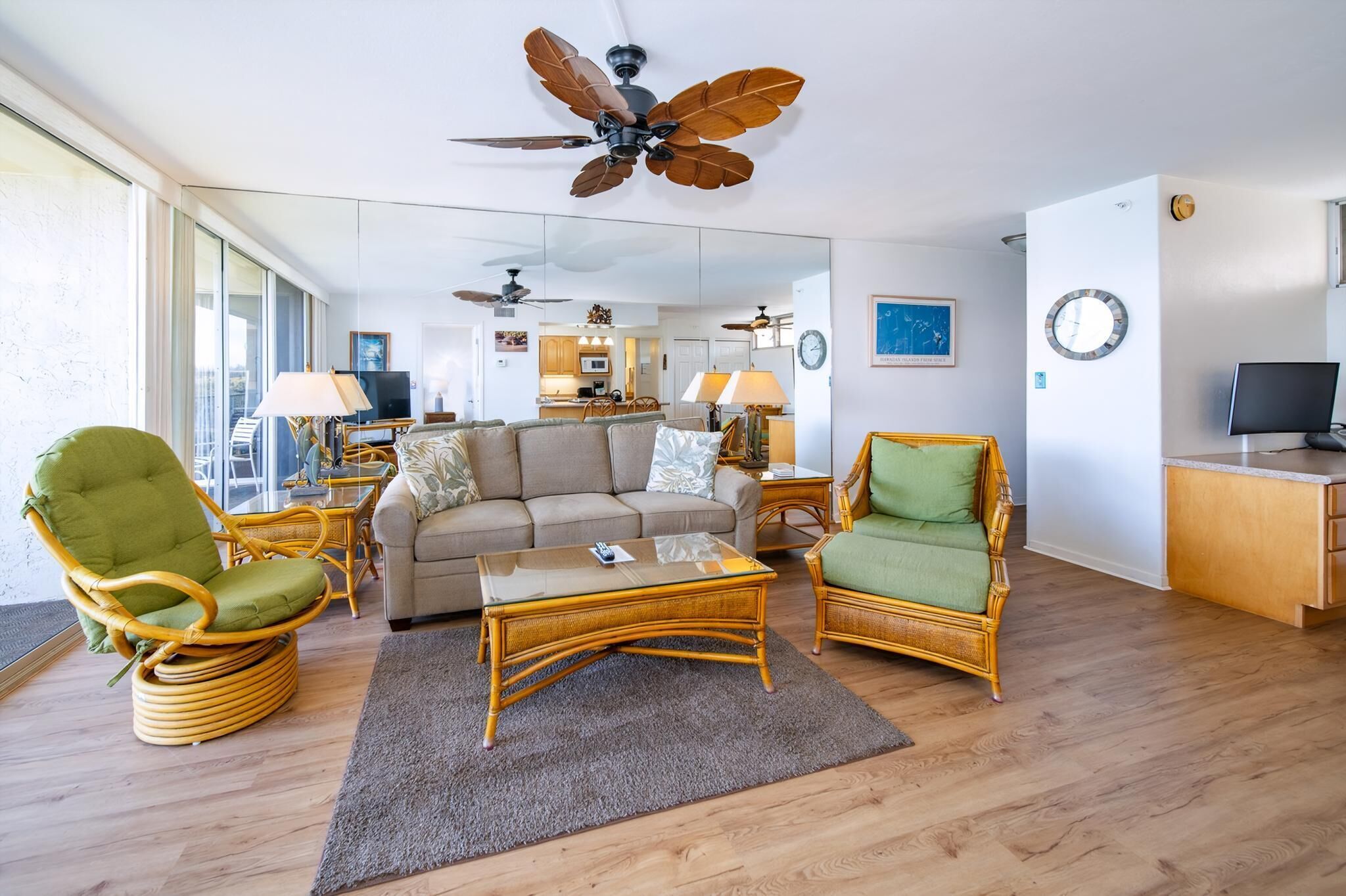 A spacious living room with a sofa, two green armchairs, a glass coffee table, and a ceiling fan.
