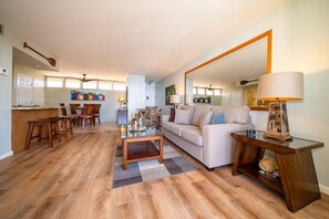 A living room with a sofa, coffee table, and a dining area with chairs. - Royal Kahana Maui 1114 Ocean View 1 Bedroom (Lahaina)