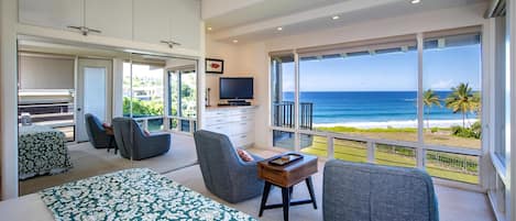 A spacious bedroom with a large bed, a balcony with a view of the ocean, and a television on a dresser.