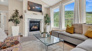 Una sala de estar con chimenea, un sofá, una mesa de centro de vidrio y un televisor sobre la chimenea.