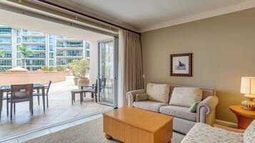 A hotel room with a sofa, armchair, coffee table, and a dining area with chairs and a table.