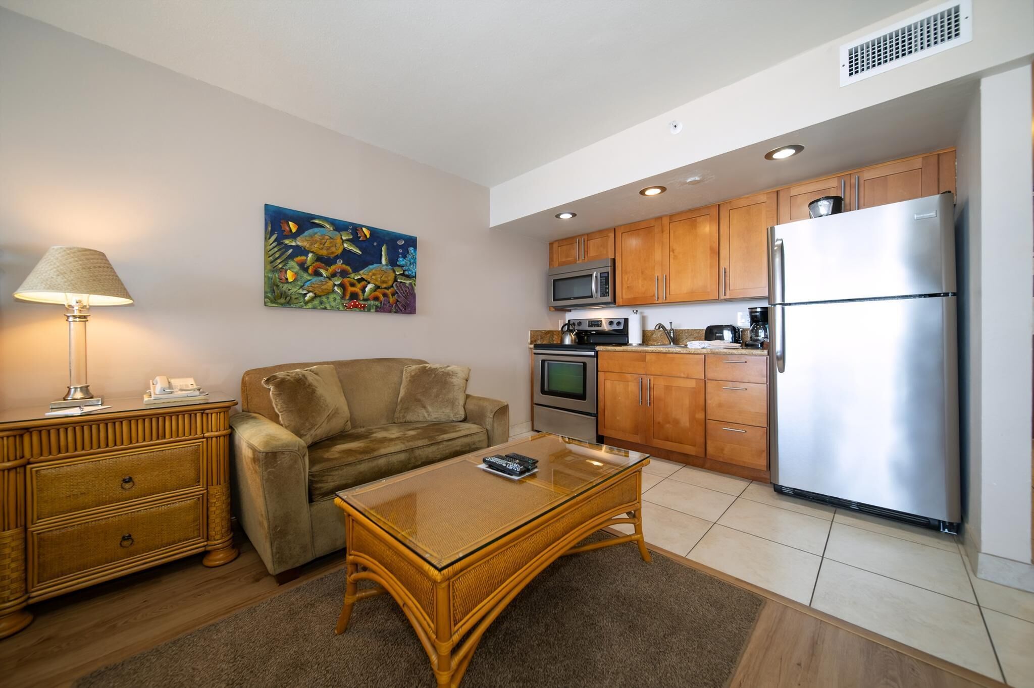 A compact living space with a sofa, coffee table, wooden cabinet, microwave, oven, and refrigerator.