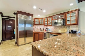 Una cocina con encimeras de granito, electrodomésticos de acero inoxidable, armarios de madera y microondas integrado.