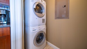 A stacked washer and dryer unit in a laundry room with a wooden cabinet and a wall-mounted electrical panel.