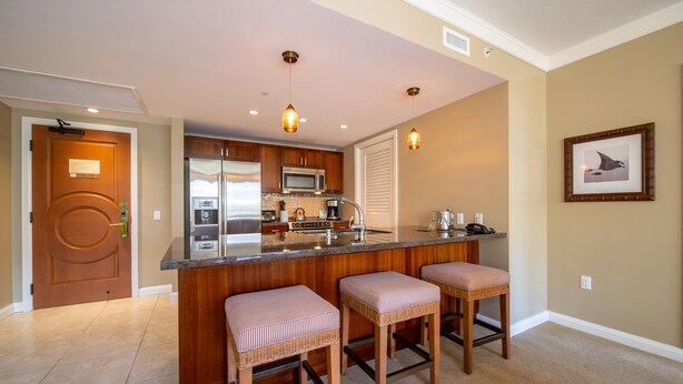 A modern kitchen with a central island, stainless steel appliances, and a wooden countertop. There are three bar stools with cushioned seats.