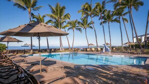 A poolside area with lounge chairs, umbrellas, and palm trees.