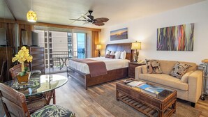 A hotel room with a bed, a sofa, a dining table with chairs, a balcony, and a painting on the wall.