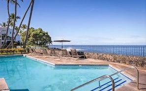 A swimming pool with lounge chairs and umbrellas, overlooking a beach with a clear view of the ocean.