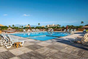 A pool area with lounge chairs and umbrellas, surrounded by palm trees and buildings.