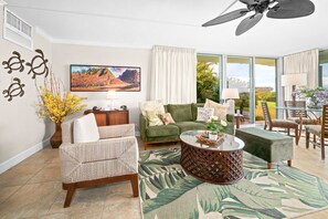 A modern living room with a sofa, armchair, coffee table, and a painting of a mountain landscape.