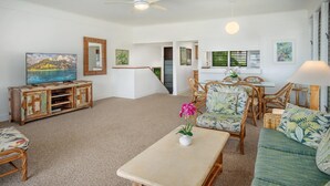 A spacious living room with a large flat-screen TV, wicker furniture, and a view of the outdoors. - Kiahuna Plantation Resort Ocean View 2 Bedroom (Koloa)