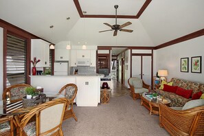 A spacious living area with a kitchen, dining table, wicker furniture, and a ceiling fan.