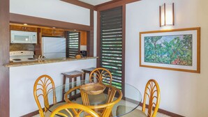 Un comedor con una mesa de vidrio, sillas de mimbre, un microondas y un refrigerador.