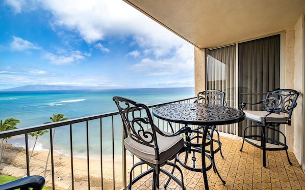 Un balcon avec une table et des chaises, donnant sur une plage et l’océan.