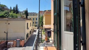 A narrow street with buildings on both sides, a balcony with a metal railing, and a clear blue sky. - 4BNB - Angelo Emo - One Bedroom Apartment, Sleeps 5 (Rome)