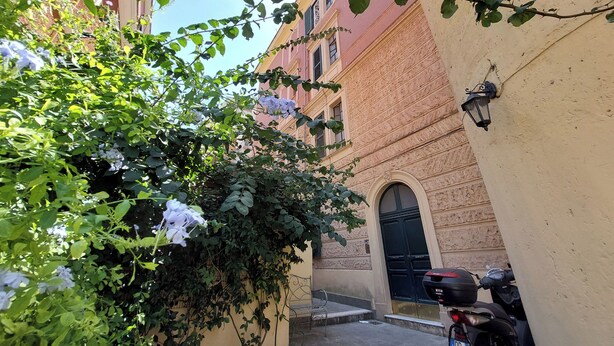 A narrow alleyway with a motorcycle parked on the right, a bench, and a building with a black door and a small hanging lantern. - 4BNB - Angelo Emo - One Bedroom Apartment, Sleeps 5 (Rome)