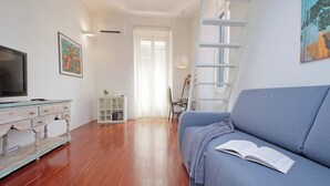 A living room with a blue sofa, a wooden coffee table, a TV, and a bookshelf. - 4BNB - Angelo Emo - One Bedroom Apartment, Sleeps 5 (Rome)