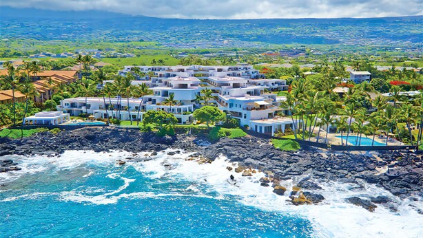 A coastal resort with multiple white buildings, a rocky shoreline, and a view of the ocean and distant landscape. - Royal Sea Cliff Kona 429 Partial Ocean View Studio (Kailua Kona)