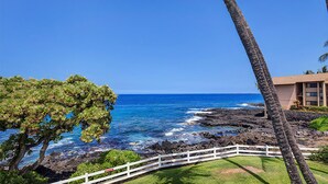 A coastal view with a white fence, a building, and a tree. - Royal Sea Cliff Kona 429 Partial Ocean View Studio (Kailua Kona)