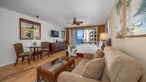 A living room with a sofa, chairs, a coffee table, a TV, a ceiling fan, and a balcony with a view. - Royal Kahana Maui 503 Ocean View Studio (Lahaina)