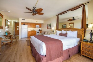 A hotel room with a large bed, a ceiling fan, a kitchen area, and a dining table.