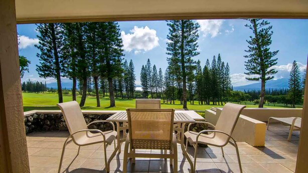 Eine überdachte Terrasse mit Tisch und Stühlen, mit Blick auf einen Golfplatz, Bäume und einen Berg in der Ferne.
