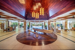 Eine großzügige Lobby mit Holzboden und einer zentral platzierten Holzskulptur eines Bootes, sowie einem modernen Kronleuchter.