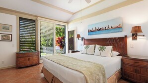 Une chambre d’hôtel avec un lit, un tableau représentant un paysage urbain, un ventilateur de plafond et une vue sur l’extérieur.