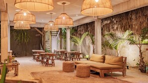 A room with a wooden sofa, round tables, and hanging wicker lamps. - Villa Mango Jeri (Jijoca de Jericoacoara)