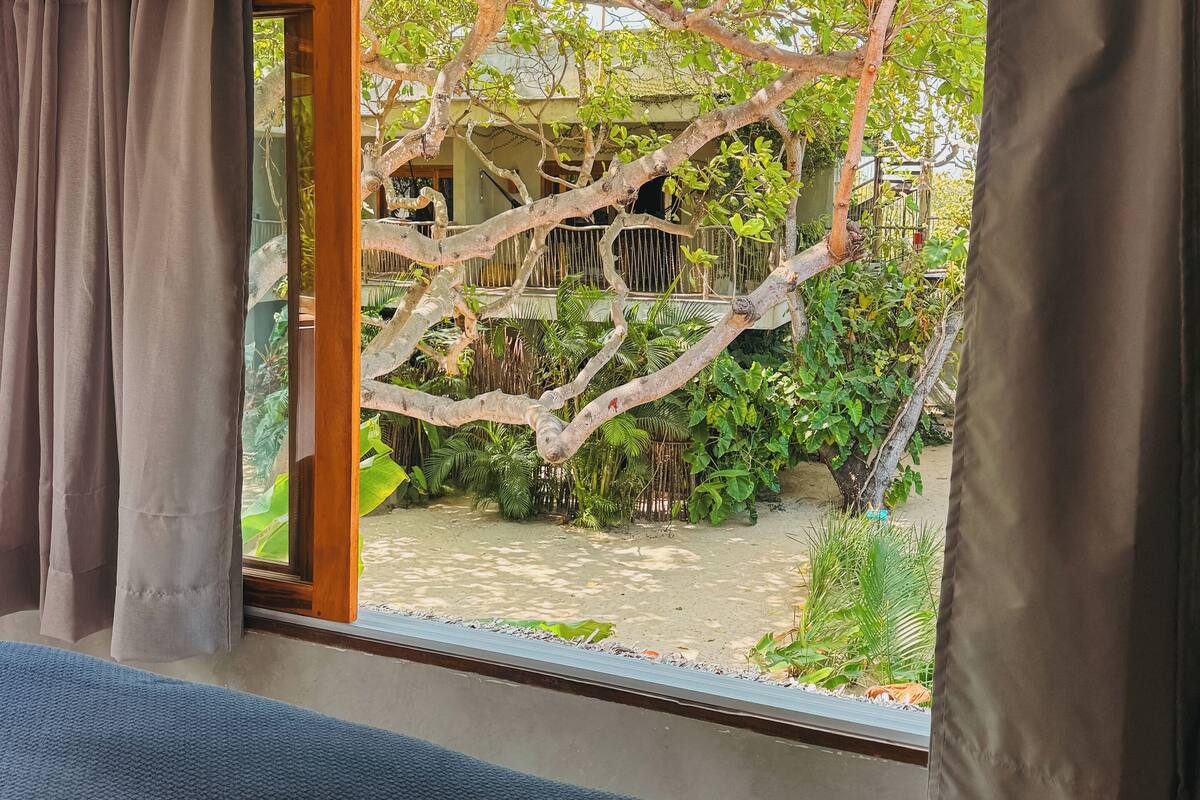 Une pièce dotée d’une grande fenêtre donnant sur un jardin avec un arbre et un petit étang.