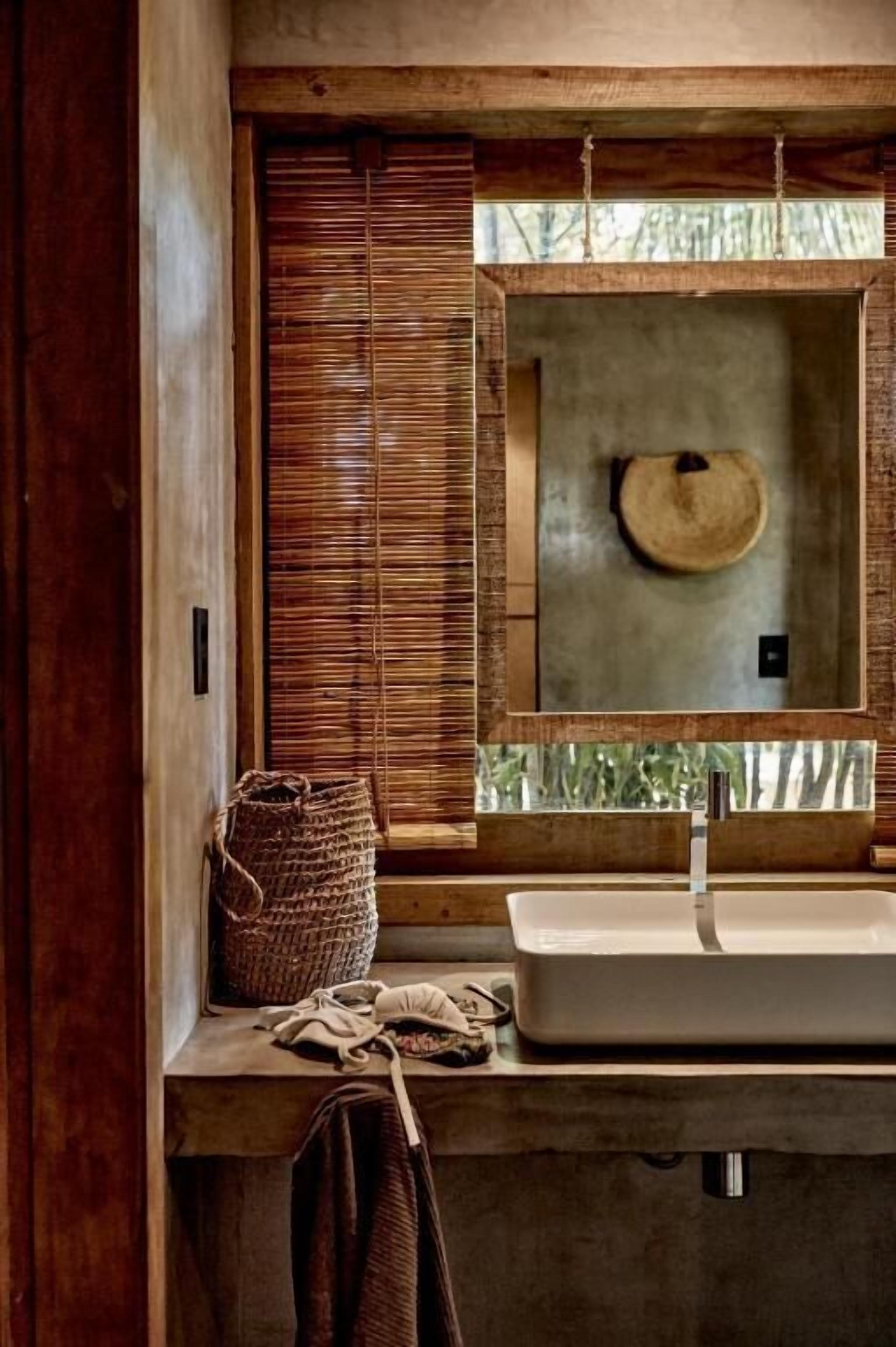 Un baño con tocador de madera, un espejo grande y una cesta tejida.