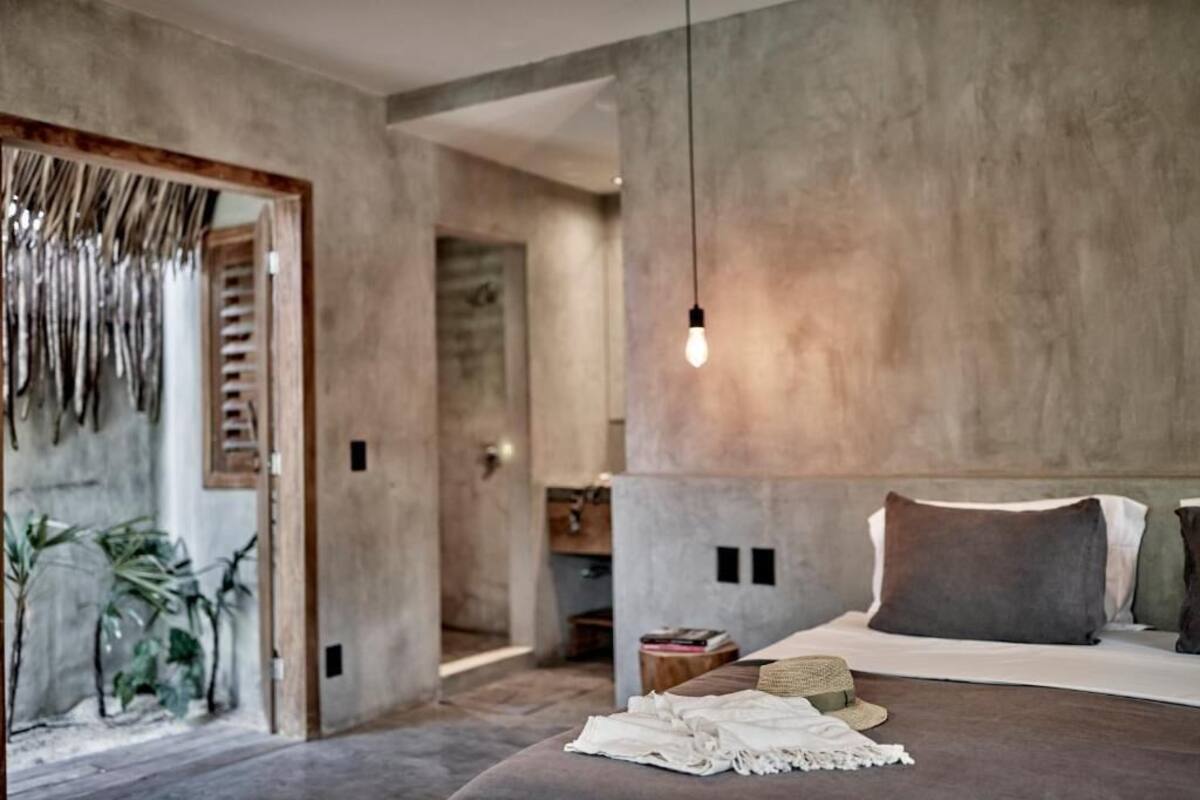 Une chambre moderne avec un grand lit, un luminaire suspendu et une vue sur un couloir agrémenté de plantes.