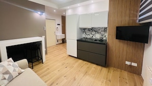 Een moderne keuken met een ingebouwde kookplaat, een spoelbak en een marmeren spatwand. Er is een flatscreen televisie aan de muur bevestigd, een houten wandpaneel en een vloer in een lichte kleur.