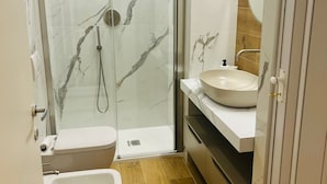 Een moderne badkamer met een douchecabine van glas, een witte wastafel en een toilet.
